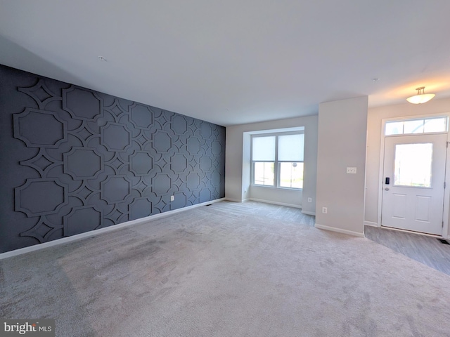 unfurnished living room with baseboards, an accent wall, carpet flooring, and wallpapered walls