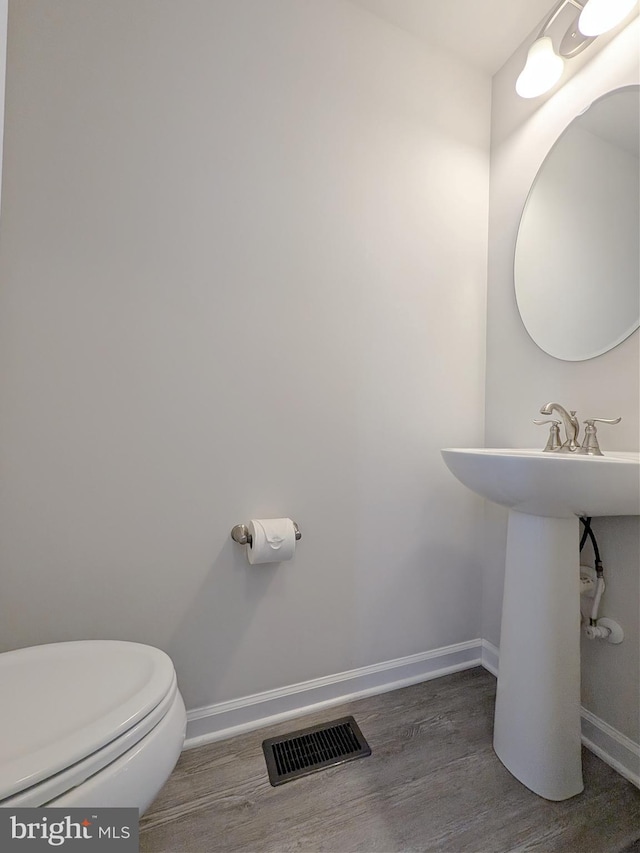 half bathroom with baseboards, toilet, wood finished floors, and visible vents