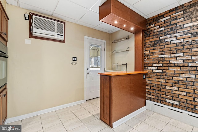 bar featuring brick wall, baseboards, a drop ceiling, an AC wall unit, and light tile patterned floors