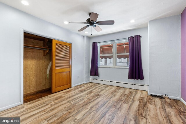 unfurnished bedroom featuring a closet, baseboards, wood finished floors, and a baseboard radiator