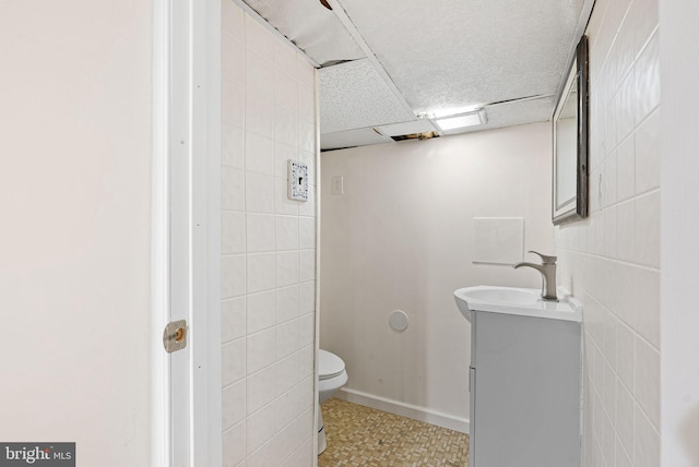 bathroom featuring vanity, baseboards, toilet, and tile walls
