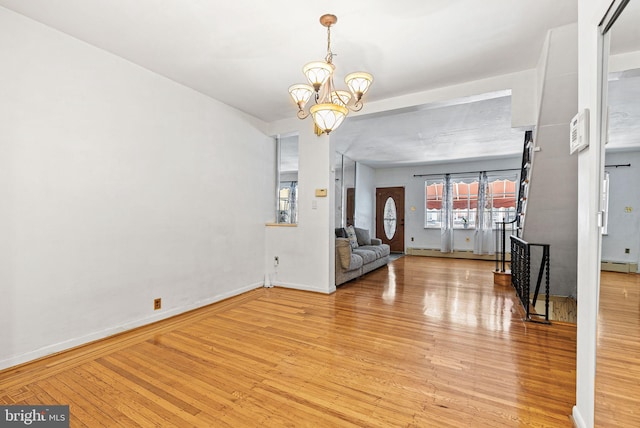foyer entrance with baseboards, a notable chandelier, baseboard heating, and wood finished floors