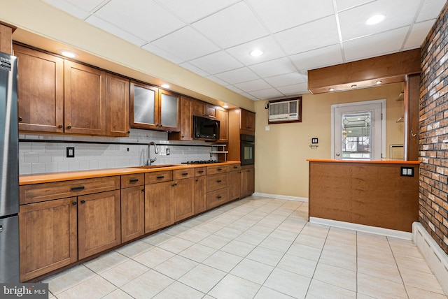 kitchen with backsplash, a paneled ceiling, brown cabinets, a sink, and black appliances