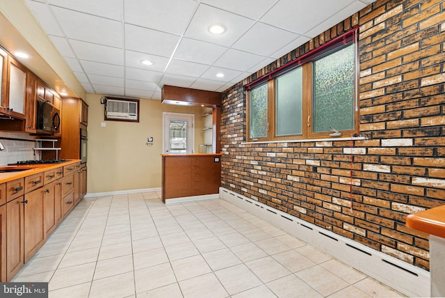 kitchen with baseboard heating, brick wall, baseboards, a drop ceiling, and black appliances