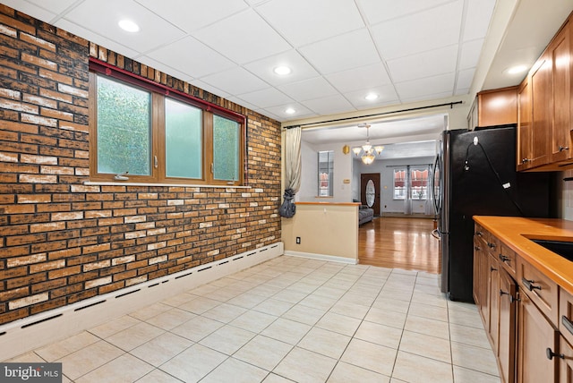 kitchen with a notable chandelier, baseboard heating, brick wall, decorative light fixtures, and a drop ceiling