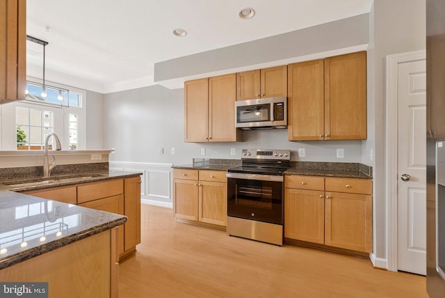 kitchen featuring a sink, appliances with stainless steel finishes, dark stone countertops, and light wood finished floors