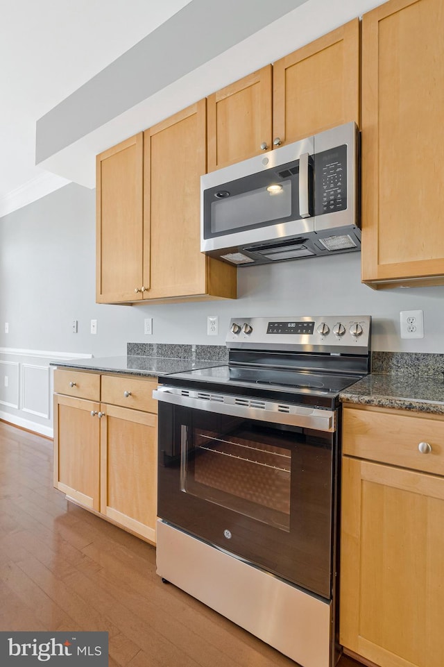 kitchen featuring a wainscoted wall, appliances with stainless steel finishes, wood finished floors, and light brown cabinets