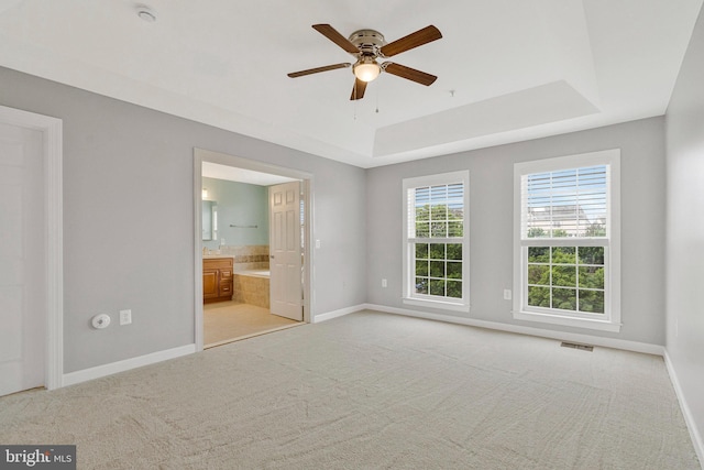 unfurnished bedroom with visible vents, light colored carpet, a raised ceiling, baseboards, and ensuite bath