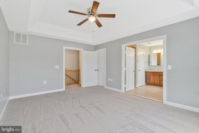 unfurnished bedroom with connected bathroom, light colored carpet, baseboards, a tray ceiling, and visible vents
