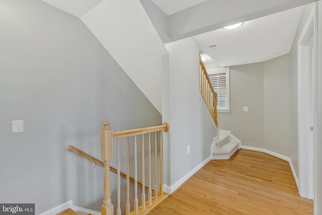 hall with baseboards, visible vents, wood finished floors, and an upstairs landing
