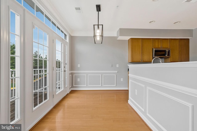 unfurnished dining area with french doors, ornamental molding, light wood-style floors, and visible vents