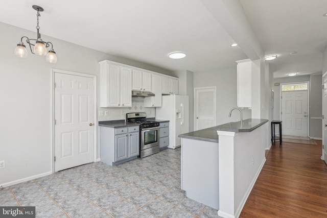 kitchen with a peninsula, dark countertops, stainless steel range with gas cooktop, under cabinet range hood, and white fridge with ice dispenser