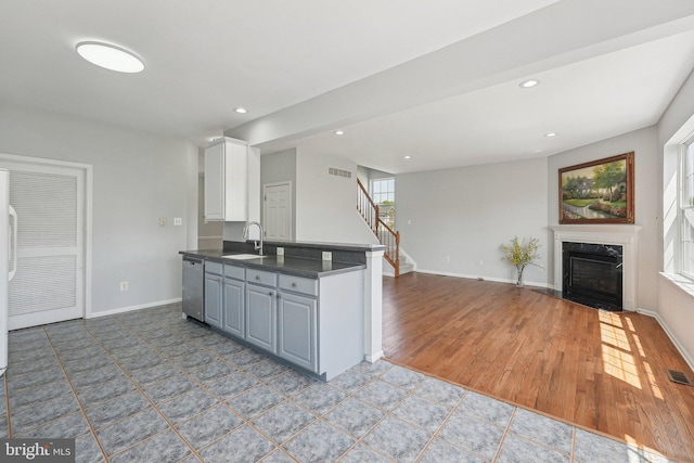 kitchen featuring a fireplace, dark countertops, baseboards, a sink, and dishwasher