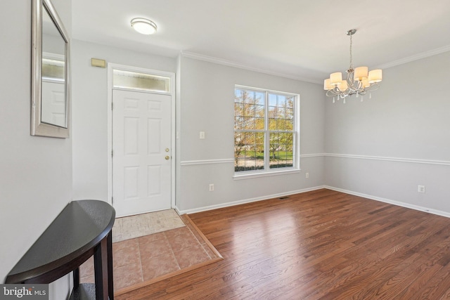 entrance foyer with baseboards, ornamental molding, wood finished floors, and a chandelier