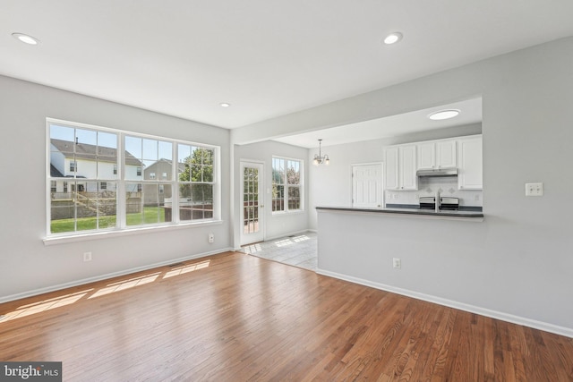 unfurnished living room featuring recessed lighting, baseboards, a notable chandelier, and wood finished floors
