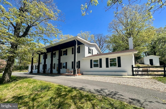 greek revival inspired property featuring brick siding, fence, and a chimney