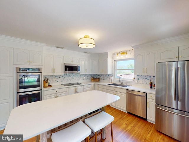 kitchen with decorative backsplash, a breakfast bar area, a sink, light wood-style flooring, and stainless steel appliances