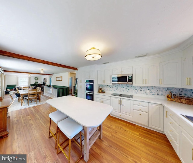 kitchen with a breakfast bar area, stainless steel appliances, light wood finished floors, and white cabinetry