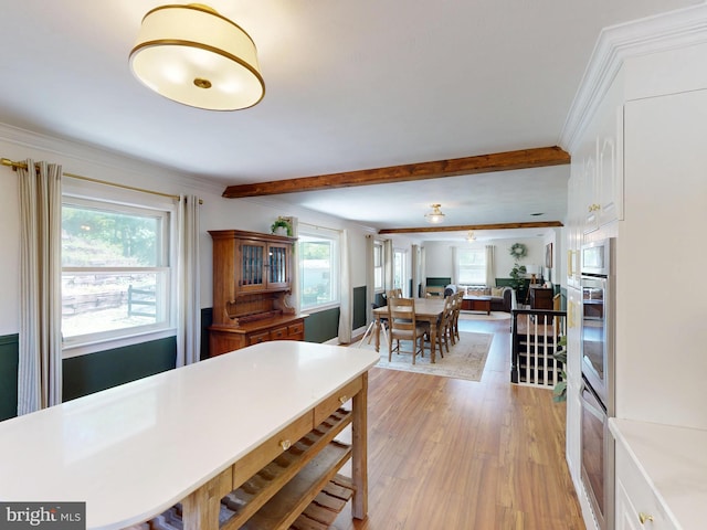 kitchen featuring oven, beamed ceiling, ornamental molding, and light wood-style floors
