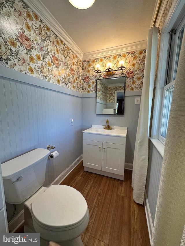 bathroom with crown molding, wood finished floors, toilet, wallpapered walls, and a wainscoted wall