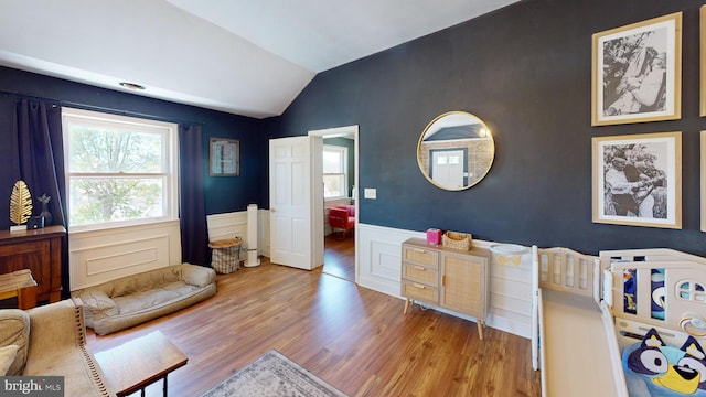 bedroom with wainscoting, wood finished floors, and lofted ceiling