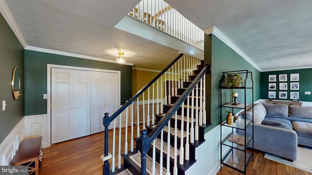 stairway featuring crown molding, wood finished floors, and a wainscoted wall