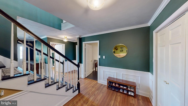 entryway featuring crown molding, wainscoting, wood finished floors, and stairway