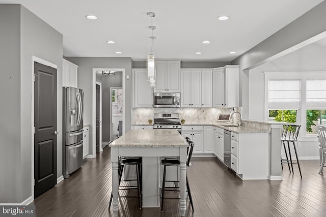 kitchen featuring a breakfast bar area, stainless steel appliances, white cabinetry, a peninsula, and tasteful backsplash