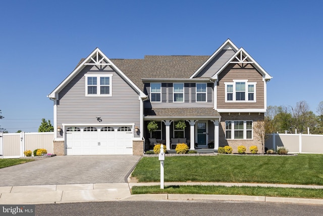 craftsman-style home featuring fence, an attached garage, a front lawn, brick siding, and decorative driveway
