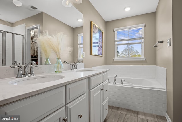 full bath with a sink, a garden tub, and a healthy amount of sunlight