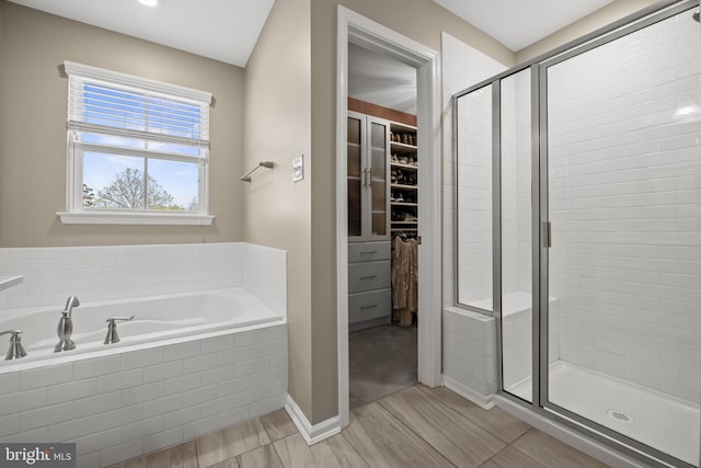 bathroom with a walk in closet, baseboards, a stall shower, and a garden tub