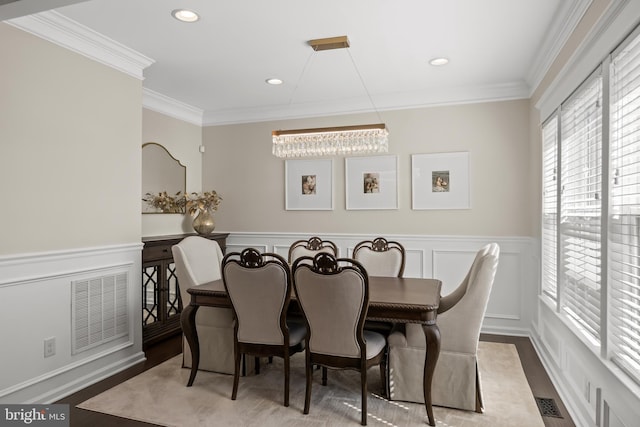 dining space featuring visible vents, crown molding, wood finished floors, a wainscoted wall, and a decorative wall