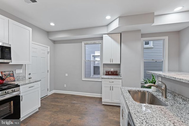 kitchen with white cabinets, dark wood-style flooring, appliances with stainless steel finishes, light stone counters, and a sink