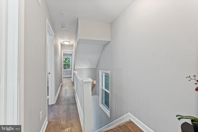 corridor with baseboards, an upstairs landing, and wood finished floors