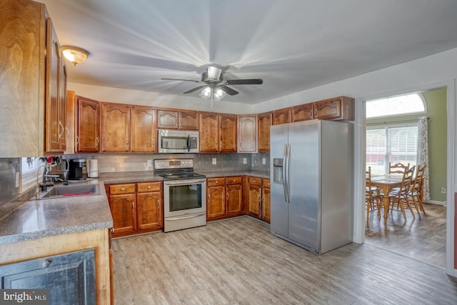 kitchen featuring appliances with stainless steel finishes, a sink, brown cabinetry, light wood-type flooring, and backsplash