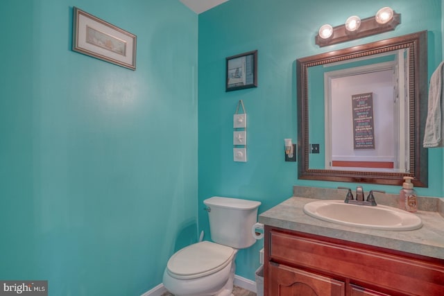 half bathroom featuring toilet, baseboards, and vanity