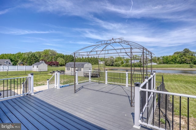 wooden deck with a water view, an outbuilding, a yard, and a storage shed