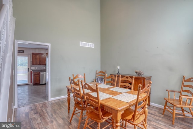 dining area with visible vents, baseboards, a towering ceiling, and wood finished floors