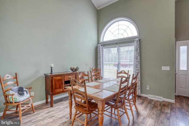 dining space with a healthy amount of sunlight, a towering ceiling, crown molding, visible vents, and wood finished floors