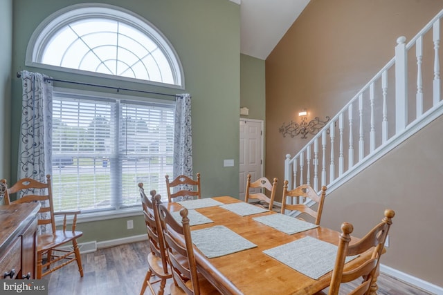 dining area with baseboards, stairs, wood finished floors, and high vaulted ceiling