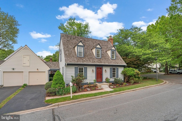 cape cod-style house featuring an outbuilding, driveway, a chimney, and a garage