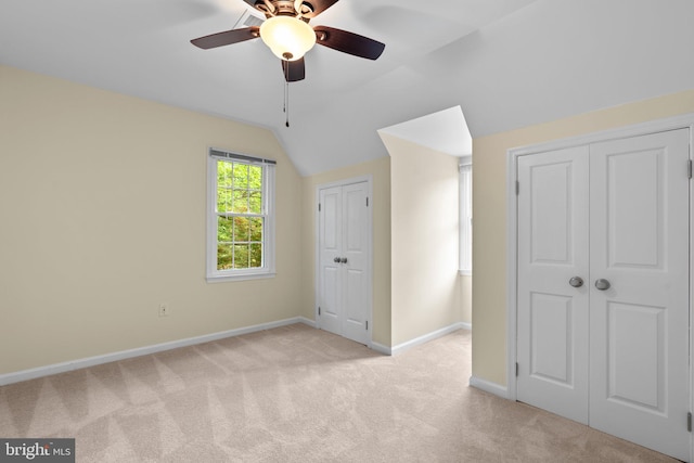 unfurnished bedroom with lofted ceiling, baseboards, two closets, and light colored carpet