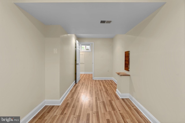 hall featuring light wood-style flooring, baseboards, and visible vents
