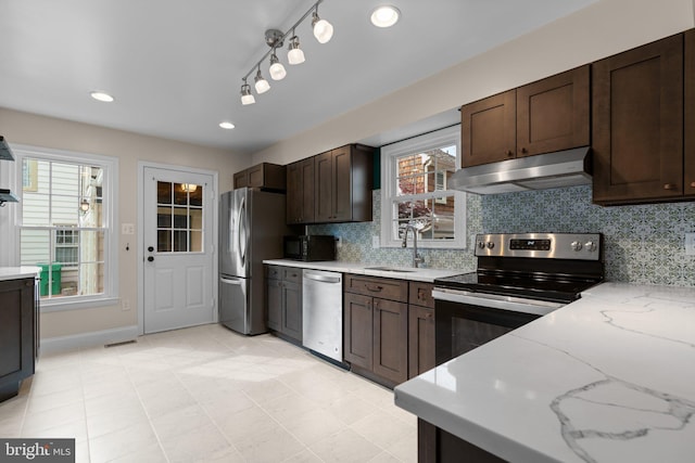 kitchen with a sink, stainless steel appliances, dark brown cabinetry, backsplash, and under cabinet range hood