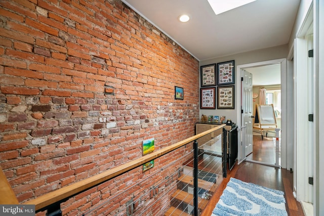 hall with recessed lighting, wood finished floors, brick wall, and an upstairs landing