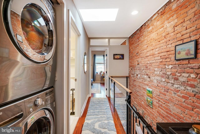 clothes washing area with laundry area, brick wall, stacked washer / dryer, and wood finished floors