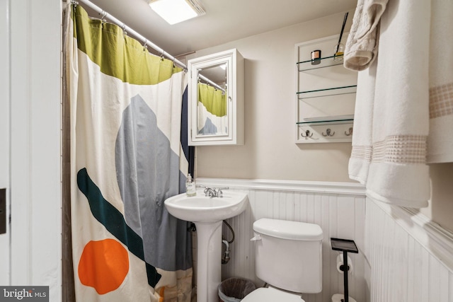 bathroom with a sink, a wainscoted wall, toilet, and a shower with shower curtain