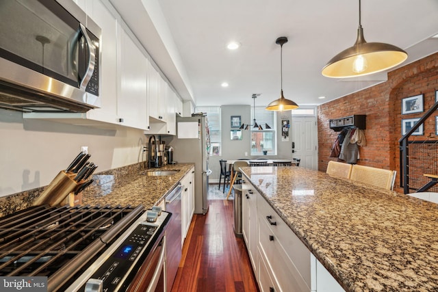 kitchen featuring dark wood-style flooring, white cabinetry, a sink, appliances with stainless steel finishes, and decorative light fixtures