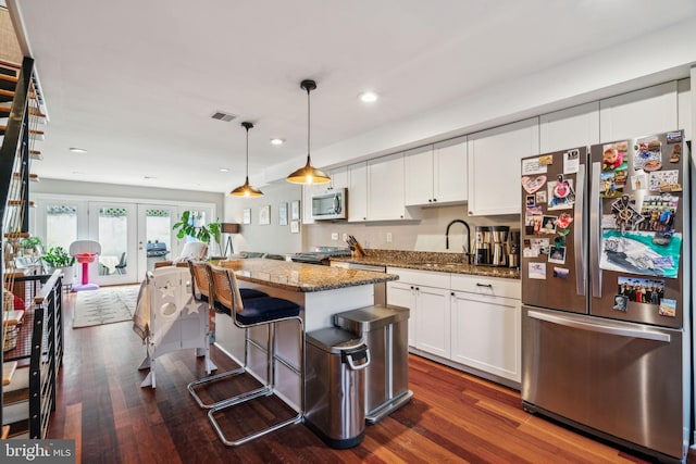 kitchen featuring visible vents, appliances with stainless steel finishes, a sink, dark wood-style floors, and dark stone counters