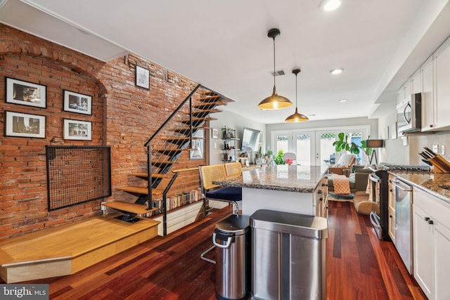 kitchen featuring stainless steel appliances, dark wood-style flooring, brick wall, and open floor plan